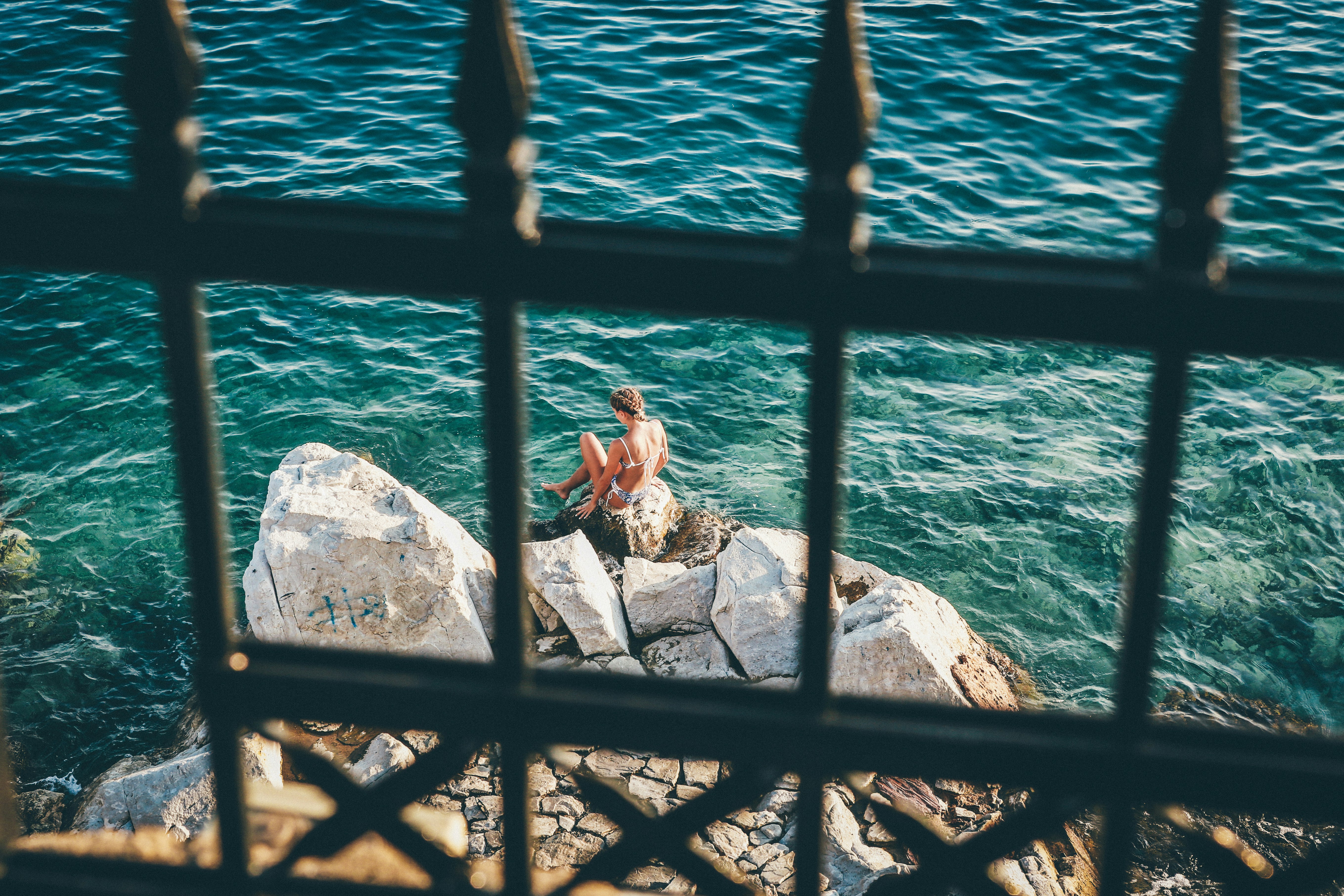 woman sitting on brown rock fragments beside body of water